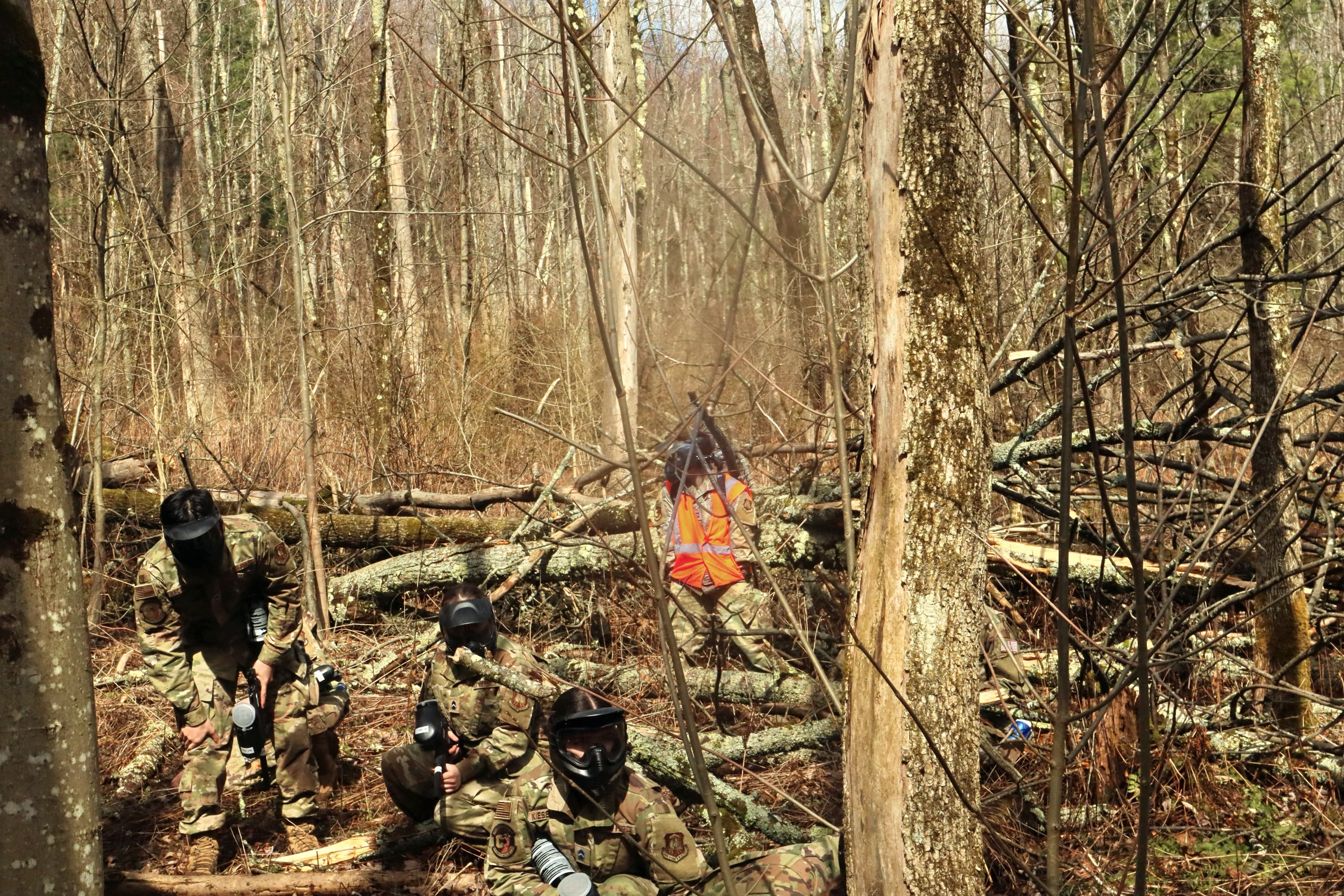 Cadets in camouflage uniforms and face paint moving through a bare winter treeline during a field training exercise.